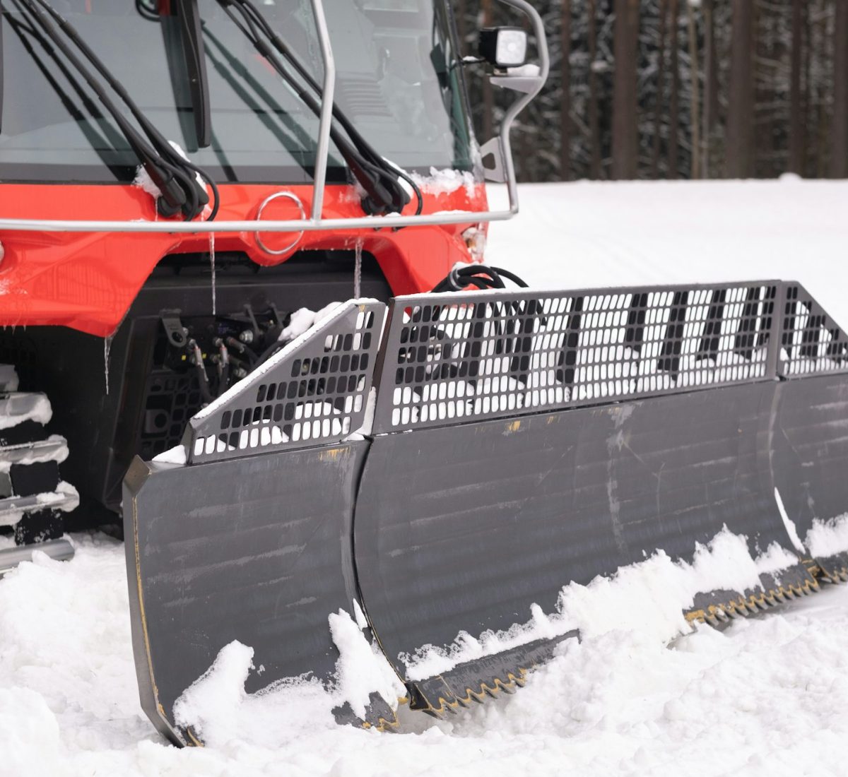 The bucket of a snowplow on tracks, standing in the forest in winter